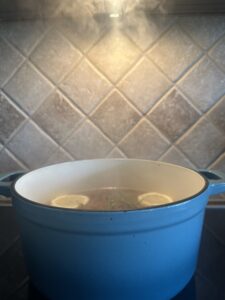 Simmer pot with lemon, rosemary, and vanilla steaming in a blue Dutch oven on a stovetop—natural summer home scent recipe.